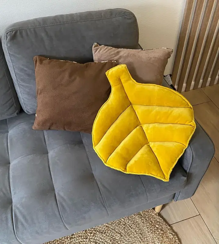 серая подушка похожая на лист на диванчике серого цвета